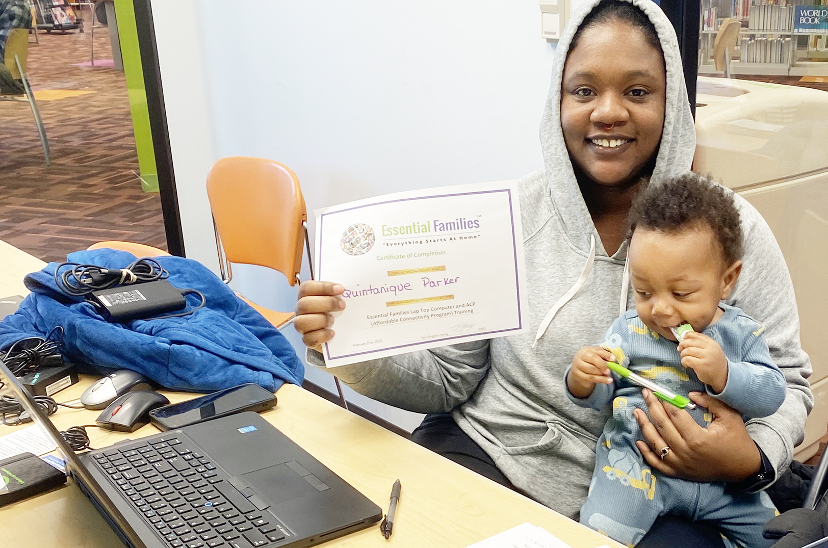 Essential Broadband Pilot participate Quintanique Parker earns her certification of completion while taking care of her young child; photo courtesy of Essential Families