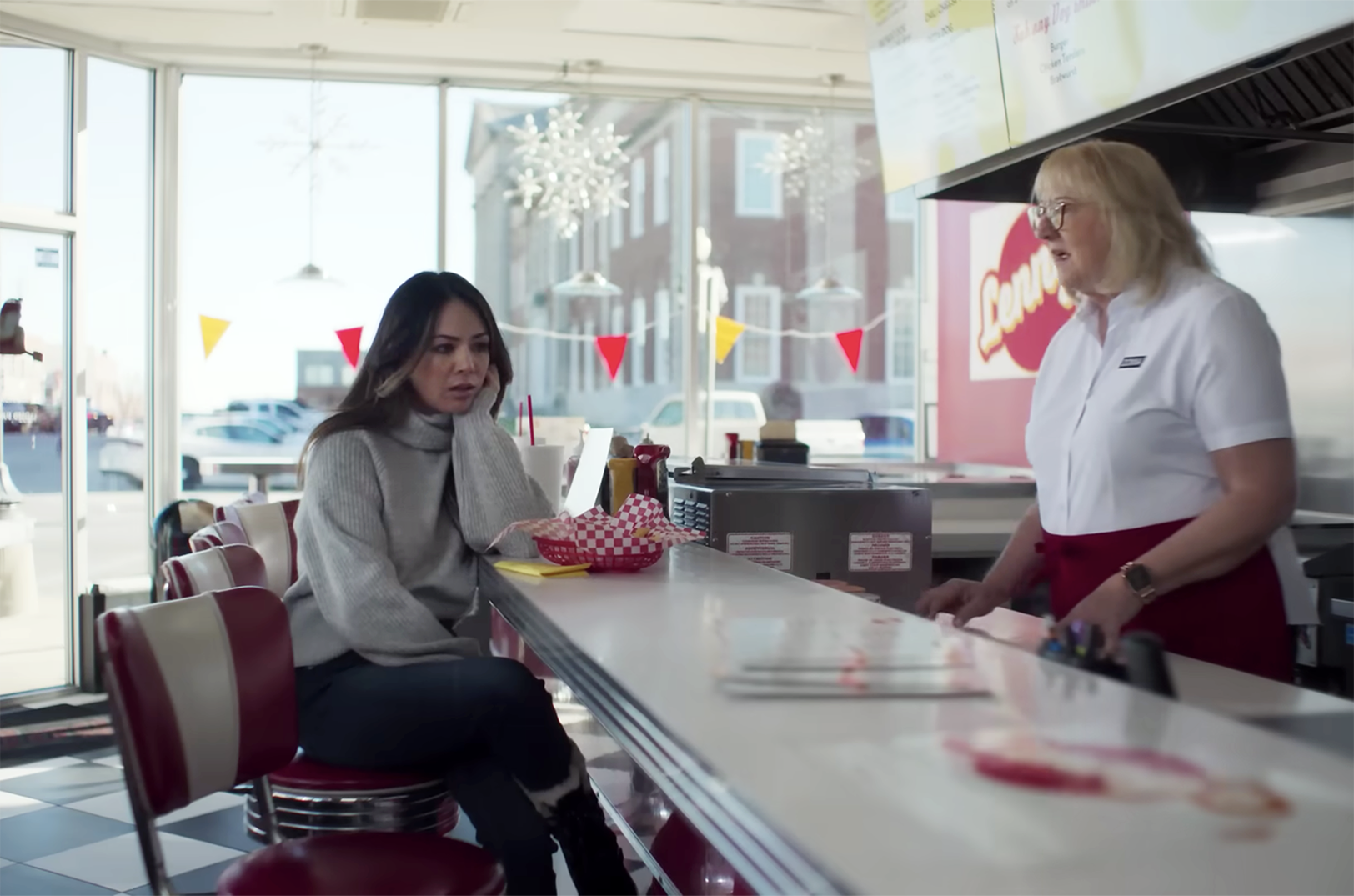 Actress Janel Parrish and Donna Kelce, the mother of the Chiefs' Travis Kelce and the Eagles' Jason Kelce, share a scene in "Falling for Football" within a mock diner with restaurant details designed by local creatives at Collective Ex; still courtesy of the Kansas City Chiefs