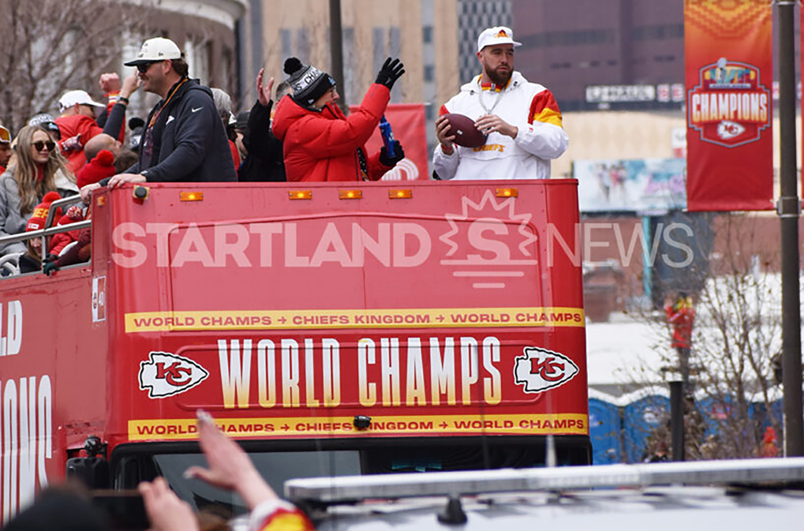 Travis Kelce prepares to toss a football to fans after signing it next to his mother during the Chiefs Super Bowl victory parade in February 2023; photo by Tommy Felts, Startland News