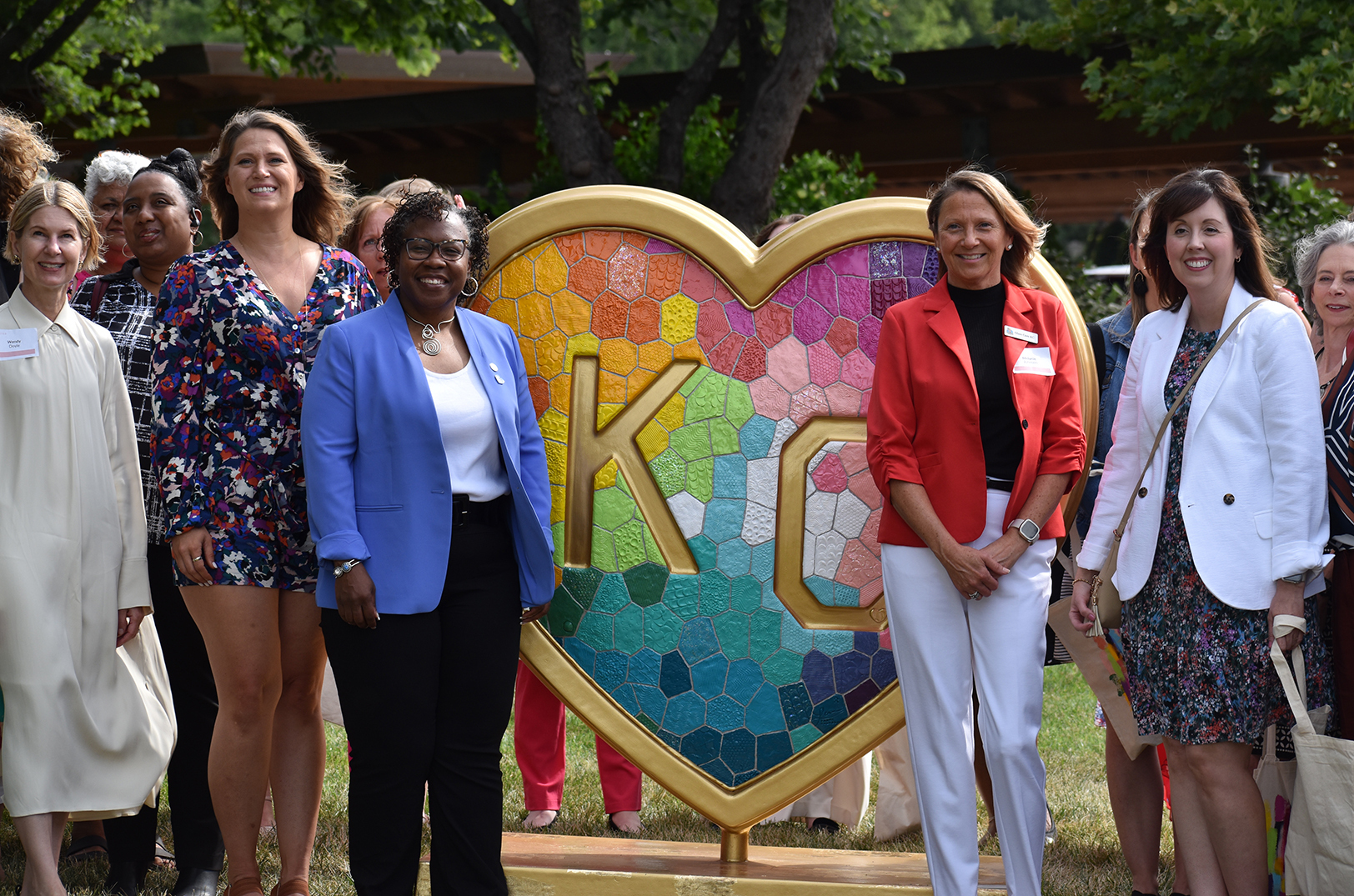 Wendy Doyle, United WE; artist Laura Crossley; and Dr. DeAngela Burns-Wallace, Ewing Marion Kauffman Foundation, all at left, stand with event attendees next to the "Takes Heart" Parade of Hearts entry on the Kauffman Foundation campus; photo by Taylor Wilmore, Startland News