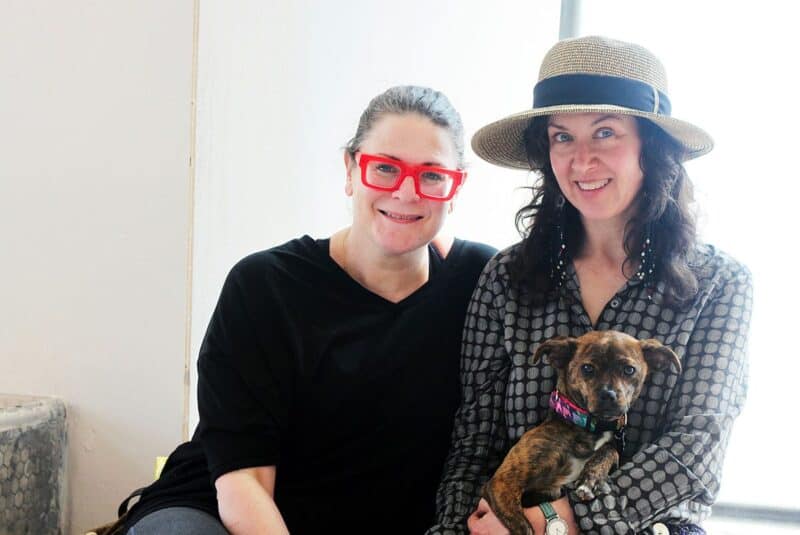 two women smiling at camera while holding a dog